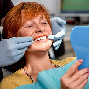 dentist showing red haired woman her teeth in mirror after cosmetic dentistry Portland, OR